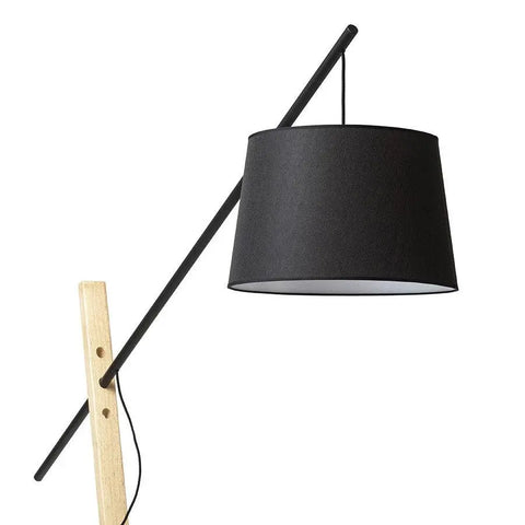 Moderni musta lattiavalaisin puujalalla, tekstiilivarjostin ja minimalistinen design, esillä valaisimen puinen kiinnitys ja sähköjohto.